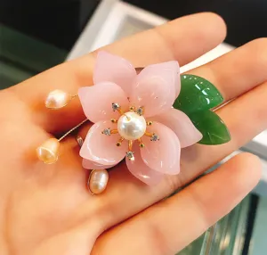 Exquisite pink flower brooch detail, featuring faux crystal petals, pearls, and green leaf.