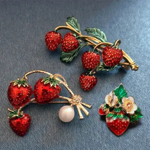 Detailopname van emaille aardbei broche met levendige rode vruchten en groene bladeren.