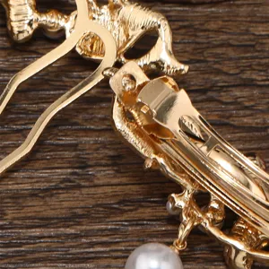 Vue détaillée de la pince à cheveux dorée avec mécanisme à ressort et pendentif perle.