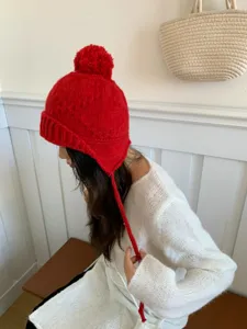 Vista detallada del gorro de punto rojo con pompón y orejeras, estilo de invierno acogedor.