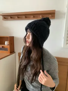 Detalle del gorro de punto negro estilo coreano con pompón y orejeras cálidas.