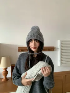 Primer plano de un gorro de punto gris acogedor con pompón y orejeras en interior.