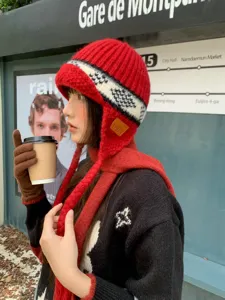 Close-up detail of the stylish red knitted ear-flap beanie hat with winter street background.