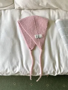 Detailansicht des rosa Strick-Ohrwärmers mit süßem Aufnäher und Bändern, weiche Textur.
