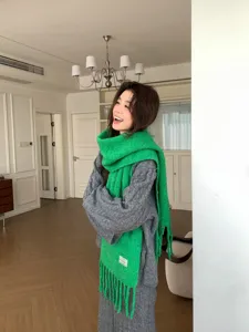 Close-up of a vibrant green knitted scarf worn by a model in a cozy indoor lifestyle setting.
