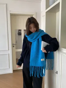 Blue knitted winter scarf with tassels worn by a model, cozy wool blend cold weather accessory