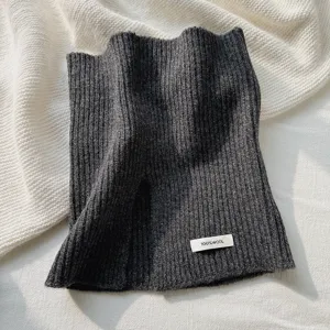 Vista detallada del calentador de cuello de punto gris oscuro con etiqueta 100% lana y textura.