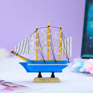 Nahaufnahme einer kleinen blauen Segelboot-Miniatur mit gelben Masten und gestreiften Segeln.