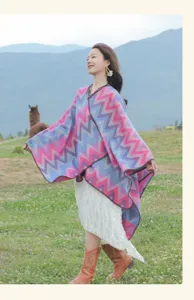 Outdoor lifestyle photo showing a colorful zigzag knitted poncho cape worn by woman in field.