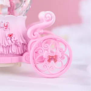 Détail de boule à neige calèche rose avec joli nœud et design de roue délicat pour déco chambre.