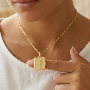 Detalle de primer plano del collar con medallón de libro chapado en oro, cruz delicada.