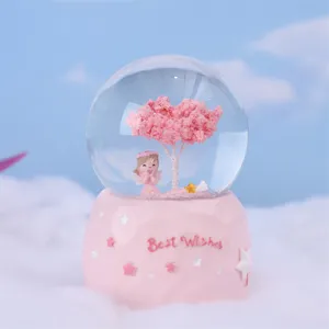 Close-up detail view of the pink crystal snow globe featuring an angel and cherry tree.