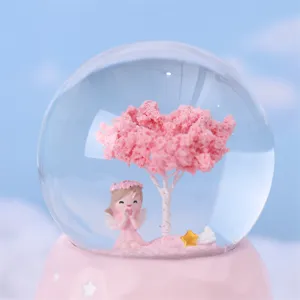 Pink crystal snow globe detail showcasing cherry tree and cute angel figurine for room decor gift.