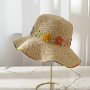 Detailansicht eines beigen Strohhutes mit bunten bestickten Blumen und breitem Rand.