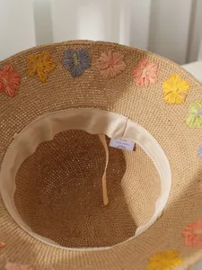 Detailansicht eines handgefertigten Strohhutes aus Papier mit bunten Bastblüten-Verzierungen.
