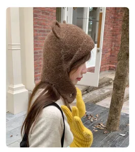 Detailaufnahme einer braunen Strickmuetze mit Baerenohren und gelben Handschuhen.