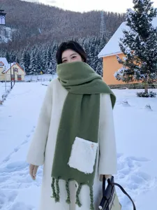 Detailansicht im winterlichen Schnee von einem dicken grunen Schal mit modischen Quasten.