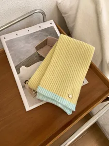 Nahaufnahme eines weichen, farbgesperrten Strickschals auf einem gemütlichen Holztablett.