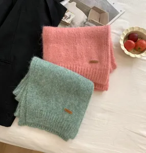 Nahaufnahme von weichen Strickschals aus Alpwollmischung in Rosa und Mint mit Lederlabel.