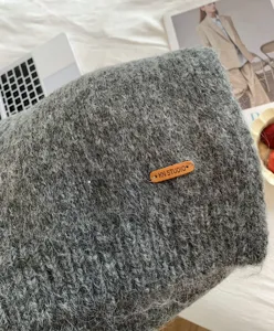 Gemütliches graues Strickschal-Detail mit weicher Alpakawolle und gebrandetem Lederetikett.