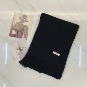 Detailansicht des dunklen Strickschals mit Fransen auf einer sauberen Marmoroberfläche.