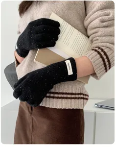 Detailansicht warmer Damen-Strickhandschuhe mit bunten Punkten, Buch in Hand, weiche Textur.