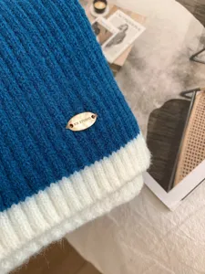 Nahaufnahme eines kuscheligen, farblich abgesetzten Strickschals mit Metall-Markenetikett.