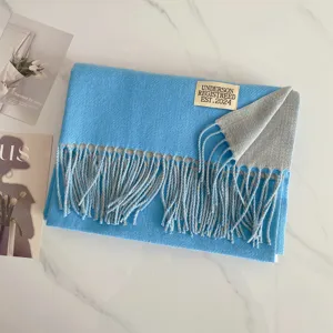 Detailaufnahme eines blauen und grauen Wende-Schals in Kaschmir-Optik mit fransigen Quasten.