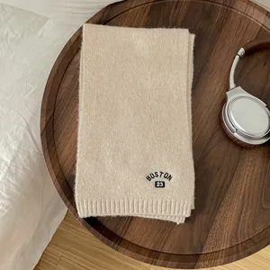 Vista dettagliata di una sciarpa in maglia beige accogliente con ricamo Boston 23 sul vassoio.