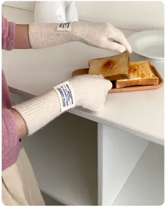 Detailed view of beige long knit gloves with wrist label, touching a wooden toast tray.