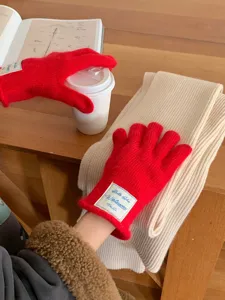 Dettaglio di guanti in maglia rossa e sciarpa beige su tavolo di legno, stile invernale accogliente.