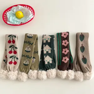 Detailed shot of children knitted cross scarf with cute patterns and plush ball pendants.