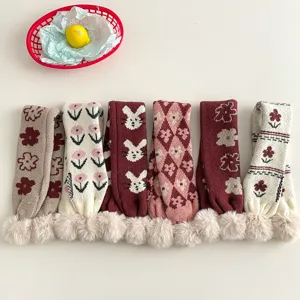 Close-up detail of children's knitted cross scarf with cute fluffy pom-pom and various patterns.
