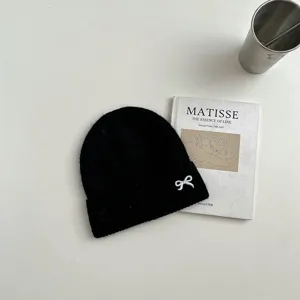Nahaufnahme einer schwarzen Strickmütze mit niedlicher weißer Schleifenstickerei, warme Mütze.