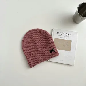 Detailansicht einer süßen rosa Strickmütze mit schwarzer Schleifenstickerei für Kinder.