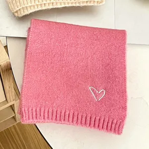 Pink knitted kids winter scarf detail with cute white heart embroidery, soft cozy texture.