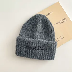 Primo piano del berretto in maglia grigio scuro con ricamo di gatto e morbida consistenza.