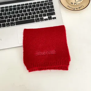 Dettaglio sciarpa invernale in maglia rossa con ricamo di lettere meoa, tessuto caldo.