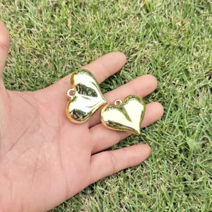 Close-up of smooth gold heart-shaped CCB pendants for DIY jewelry making in palm.