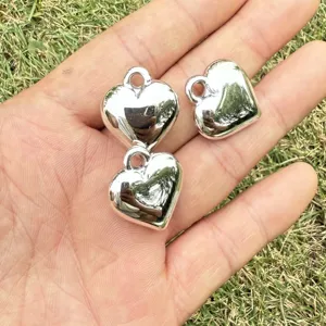 Detailed view of three polished silver CCB heart charms held in hand for size comparison