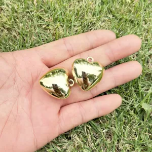 Two high-gloss golden heart-shaped CCB charms for DIY jewelry making held in hand.