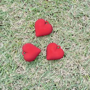 Three matte red heart-shaped charms for DIY jewelry making placed on a grass background