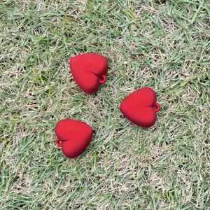 Macro detail of three vibrant matte red heart-shaped pendants on natural grass background