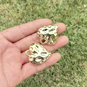 Detail view of two gold-colored CCB heart pendants with embossed texture.