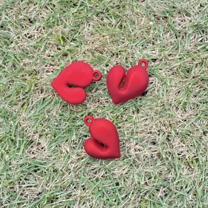 Set of three red matte heart-shaped DIY charms for jewelry making, shown on green grass.