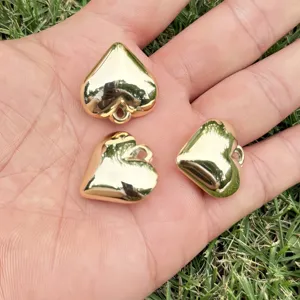Detailed view of three polished golden heart-shaped CCB charms held in palm for scale