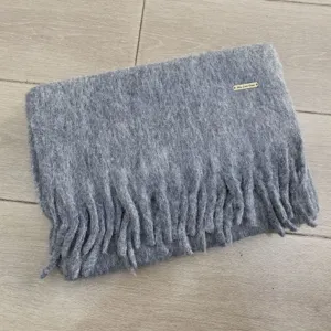 Grauer Wollmischung flauschiger Winterschal Detail Nahaufnahme, dicke Fransen und kuschelig.