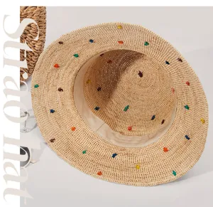 Detailansicht des sommerlichen handgemachten Bast-Strohhutes mit bunten Stickereien am Strand.