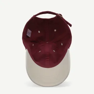Vista detallada de gorra de béisbol bicolor, copa burdeos y visera beige con hebilla ajustable.