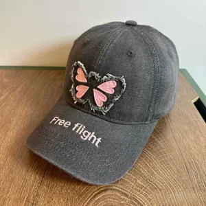 Nahaufnahme der Destroyed Jeans Baseballcap mit rosa Schmetterlingsstickerei und Textdetail.